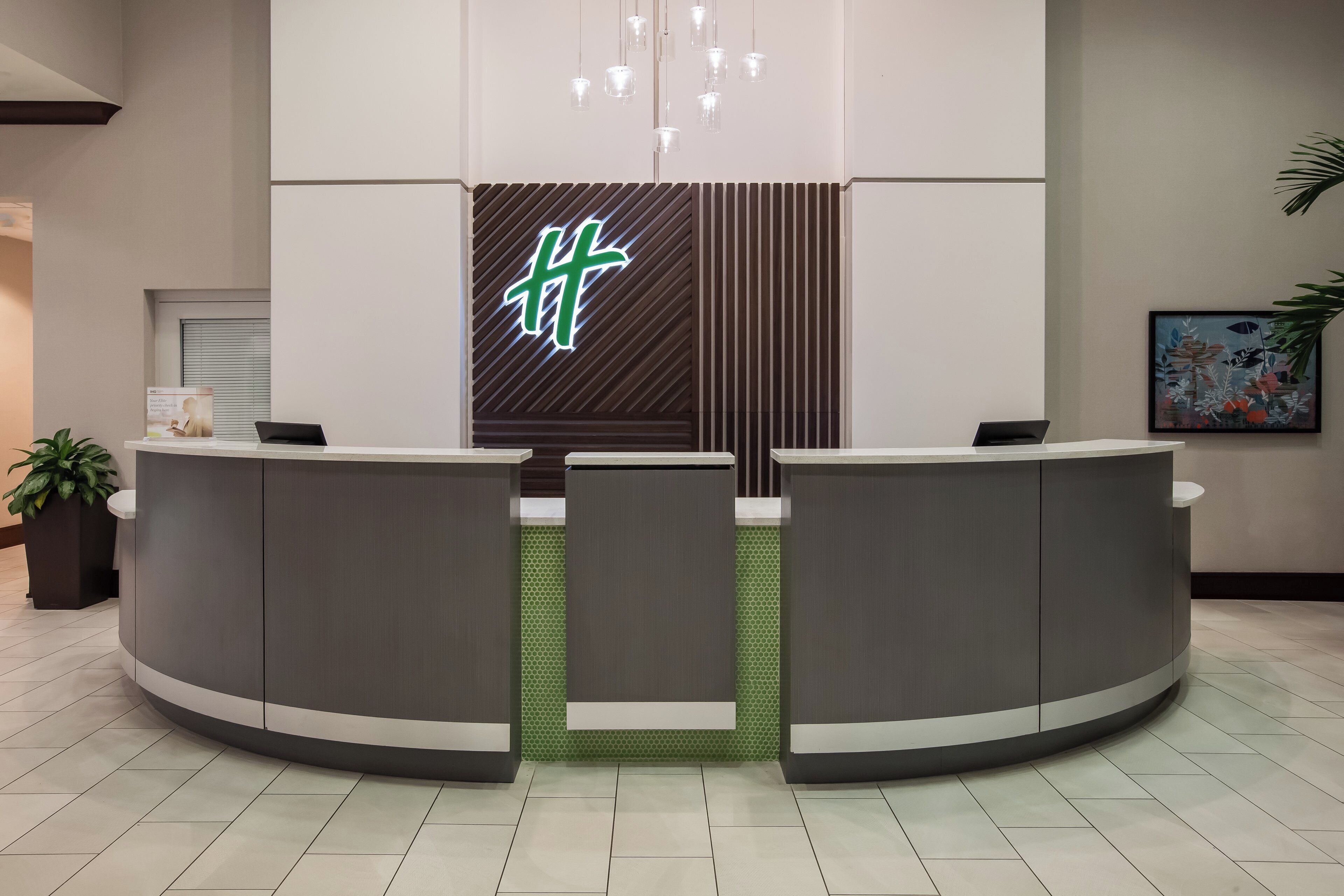 A reception area with a modern design, featuring a reception desk, a green patterned wall, and a hanging light fixture.