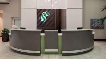 Zona de recepción con diseño moderno, que incluye un mostrador de recepción, una pared con estampado verde y una lámpara colgante.