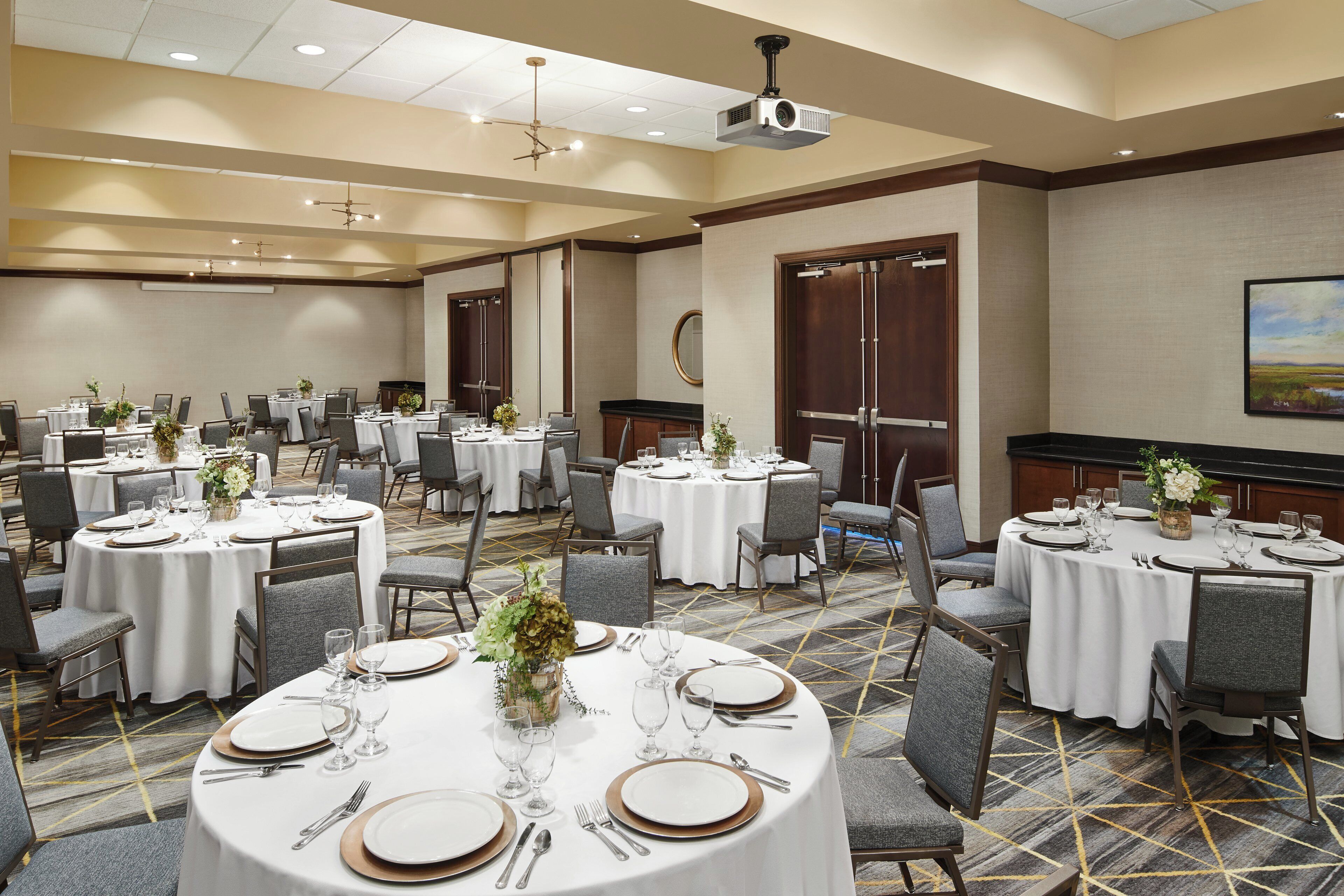 Un salón de conferencias con varias mesas dispuestas para comer, equipado con sillas, platos, cubiertos y vasos.