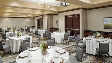 Un salón de conferencias con varias mesas dispuestas para comer, equipado con sillas, platos, cubiertos y vasos.