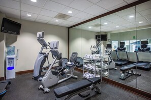 Een sportschool met diverse fitnessapparaten, waaronder loopbanden, hometrainers en een bankje.
