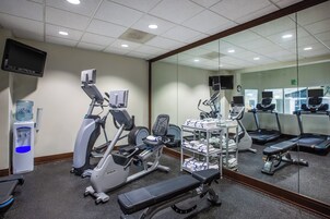 Un gimnasio con diversos equipos de ejercicio, incluyendo cintas de correr, bicicletas estáticas y una banca.
