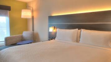 A hotel room with a large bed, a chair, a bedside table, and a lamp.