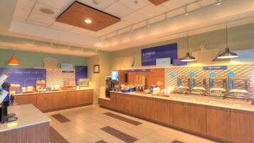 A breakfast buffet area with multiple food stations, including fruit, cereal, and hot food options.