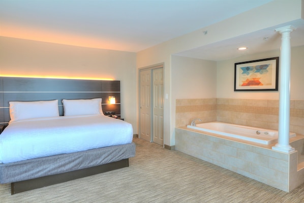 A hotel room with a large bed, a bathroom with a bathtub, and a framed picture on the wall. - Holiday Inn Express Hotel & Suites Mobile/Saraland by IHG (Saraland)