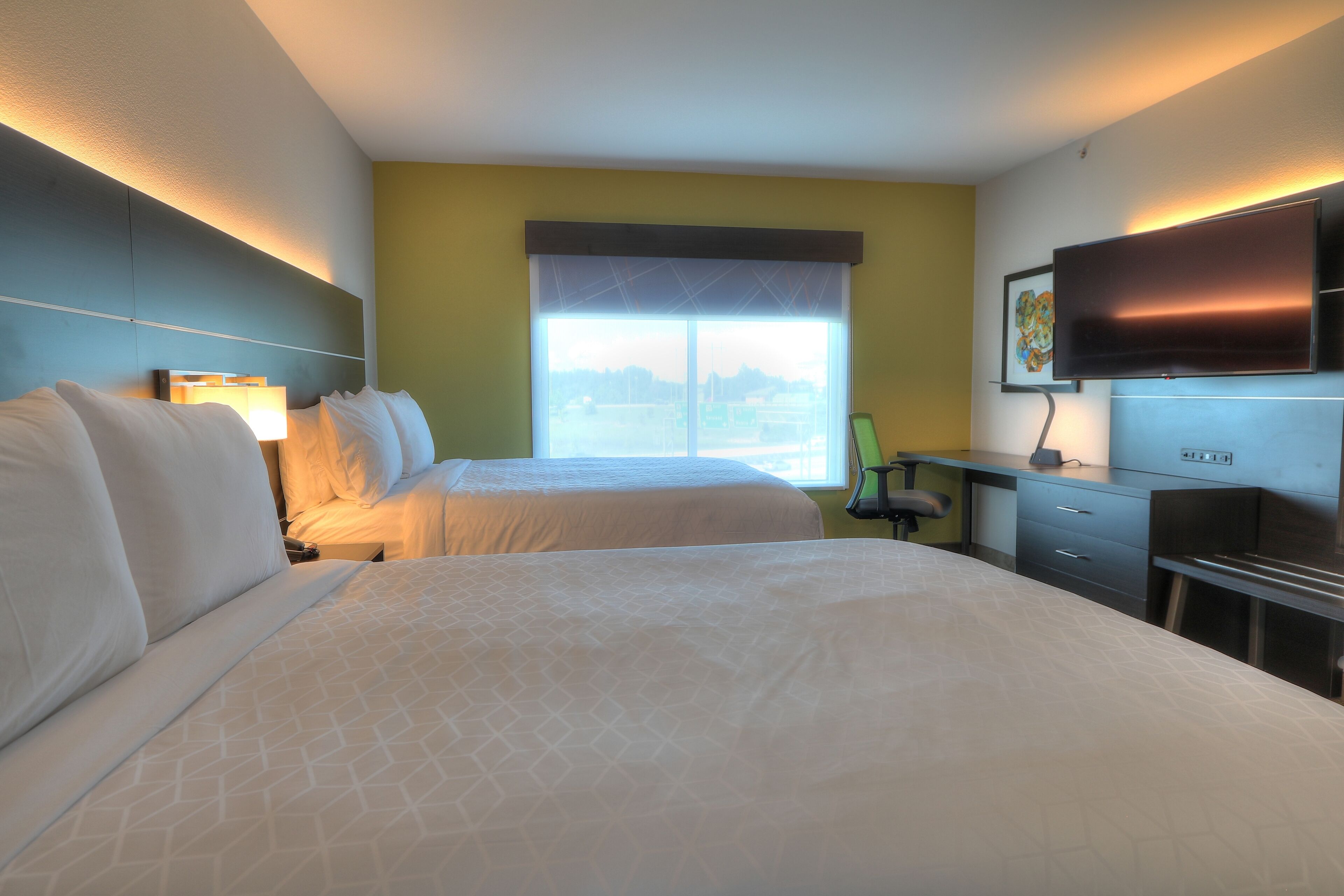 Habitación de hotel con dos camas, un escritorio con una silla, un televisor de pantalla plana y una ventana con vistas.