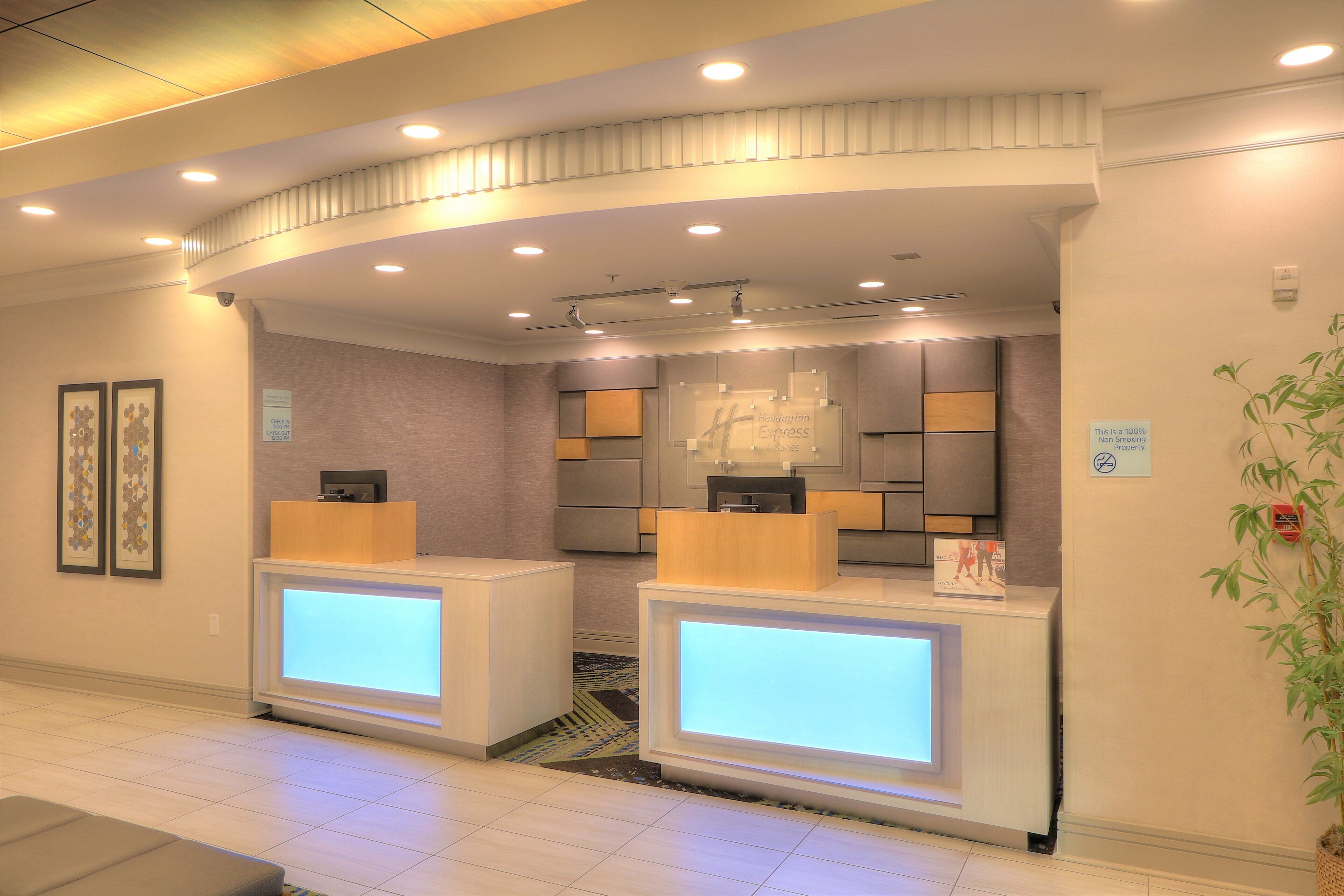 A hotel reception area with two reception desks, a check-in counter, and a wall-mounted sign indicating a 100% non-smoking property.