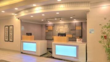 A hotel reception area with two reception desks, a check-in counter, and a wall-mounted sign indicating a 100% non-smoking property.