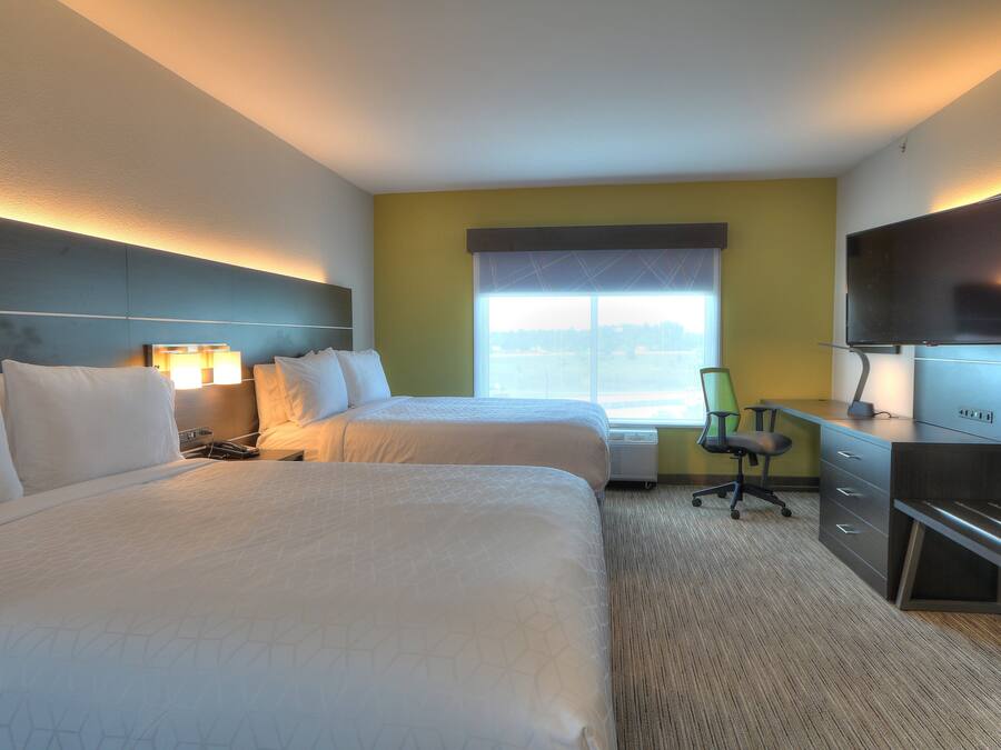 A hotel room with two beds, a desk, a chair, a TV, and a window with a view.