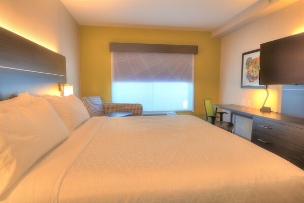 A hotel room with a large bed, a desk, a chair, and a television.