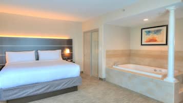 A hotel room with a bed, a bedside table, a lamp, a door, and a bathroom with a bathtub and a towel rack.