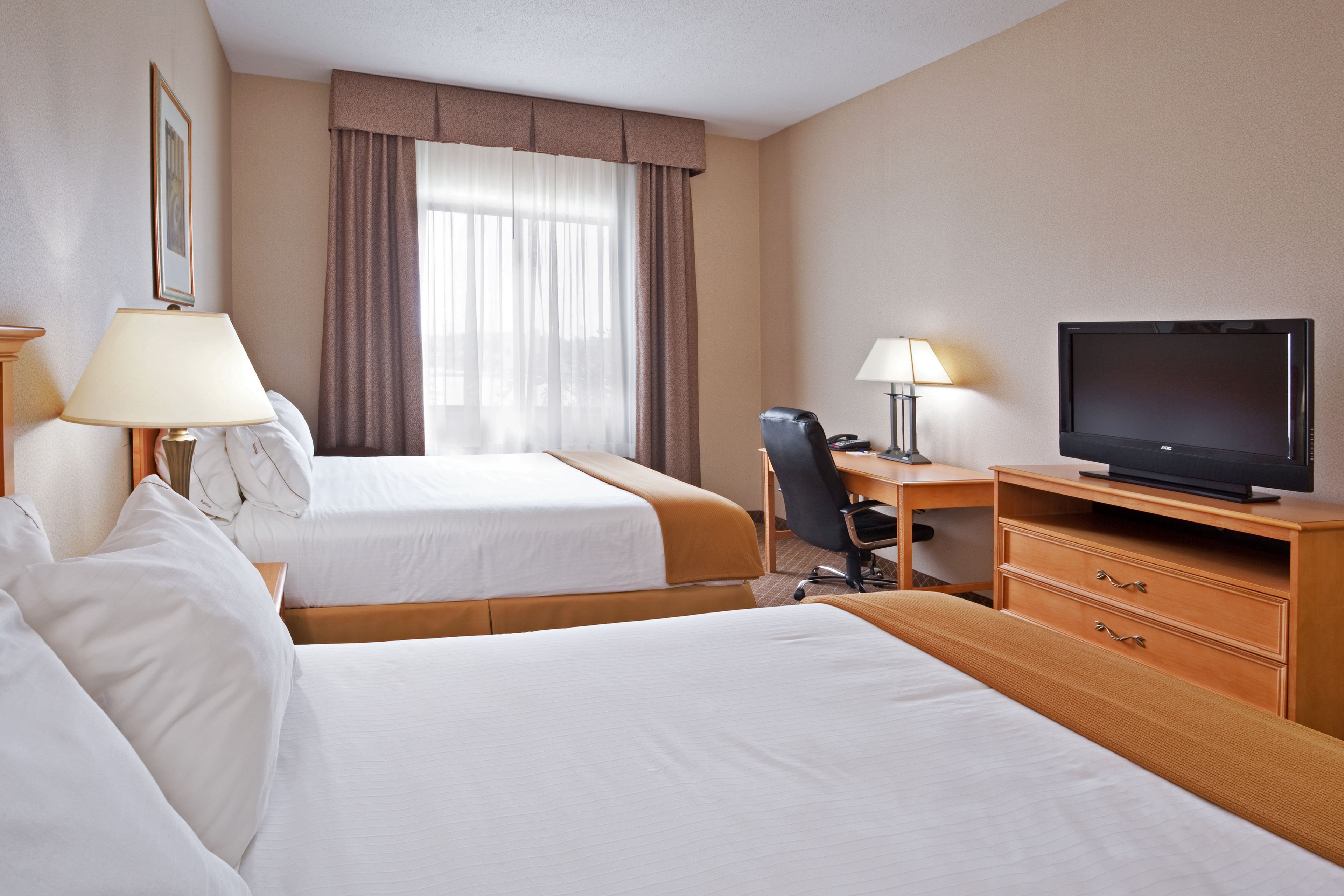 Ein Hotelzimmer mit zwei Betten, einem Schreibtisch mit Stuhl, einem Fernseher und einer Lampe.