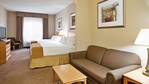 A hotel room with a bed, a sofa, a table, a TV, and a painting on the wall.
