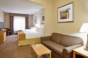 A hotel room with a bed, a sofa, a table, a TV, and a painting on the wall.