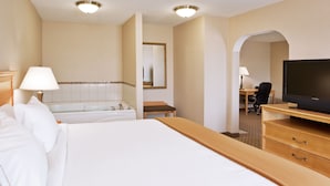 A hotel room with a large bed, a TV on a wooden dresser, a desk with a chair, and a bathroom with a bathtub and mirror.