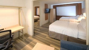 Ein Hotelzimmer mit Schreibtisch, zwei Betten, einem Fernseher und einem großen Fenster.
