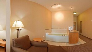 A hotel room with a sofa, a lamp, a small table, a bathtub, and a wooden counter.