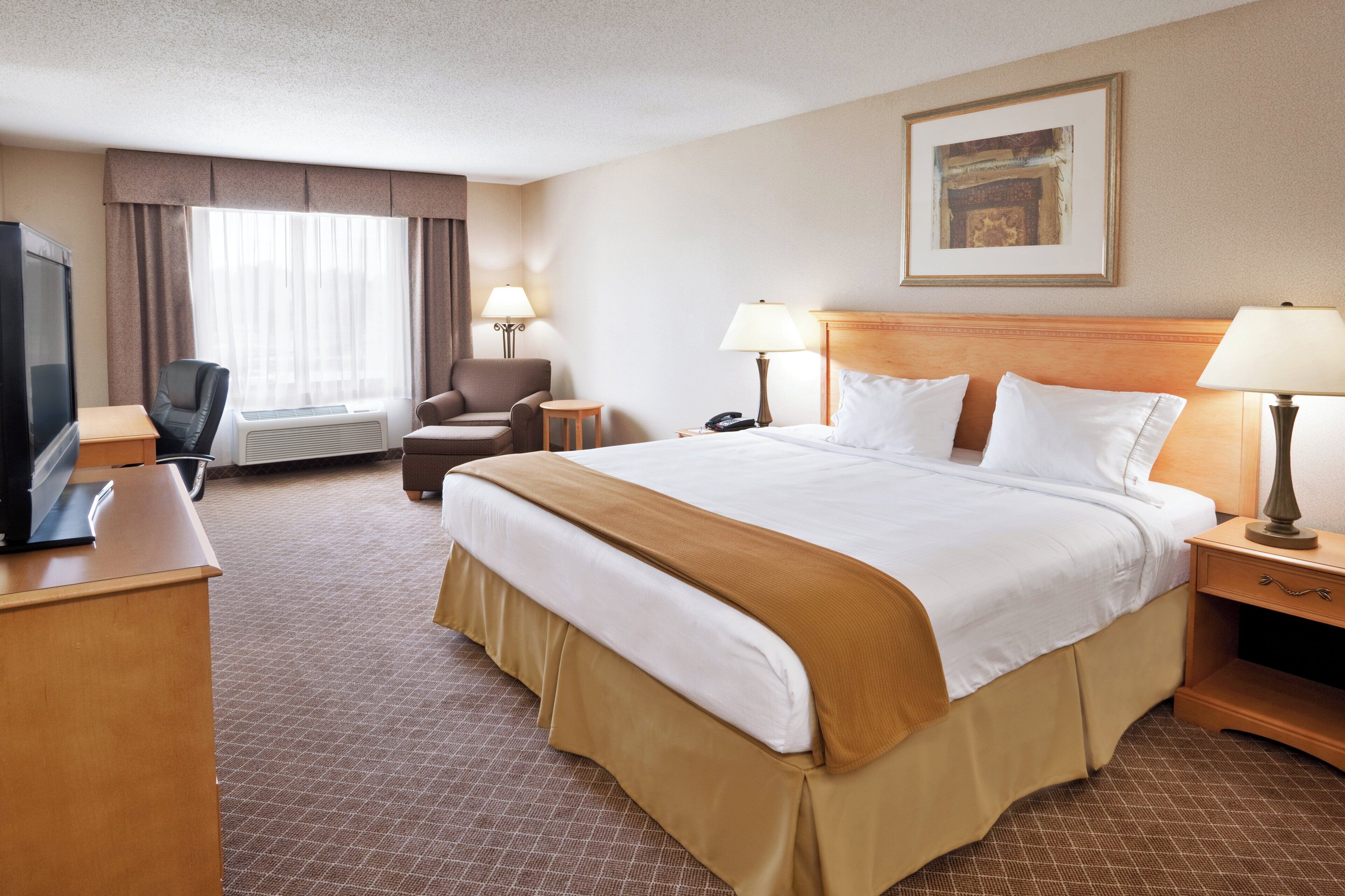 A hotel room with a bed, a desk, a chair, a television, and a lamp.