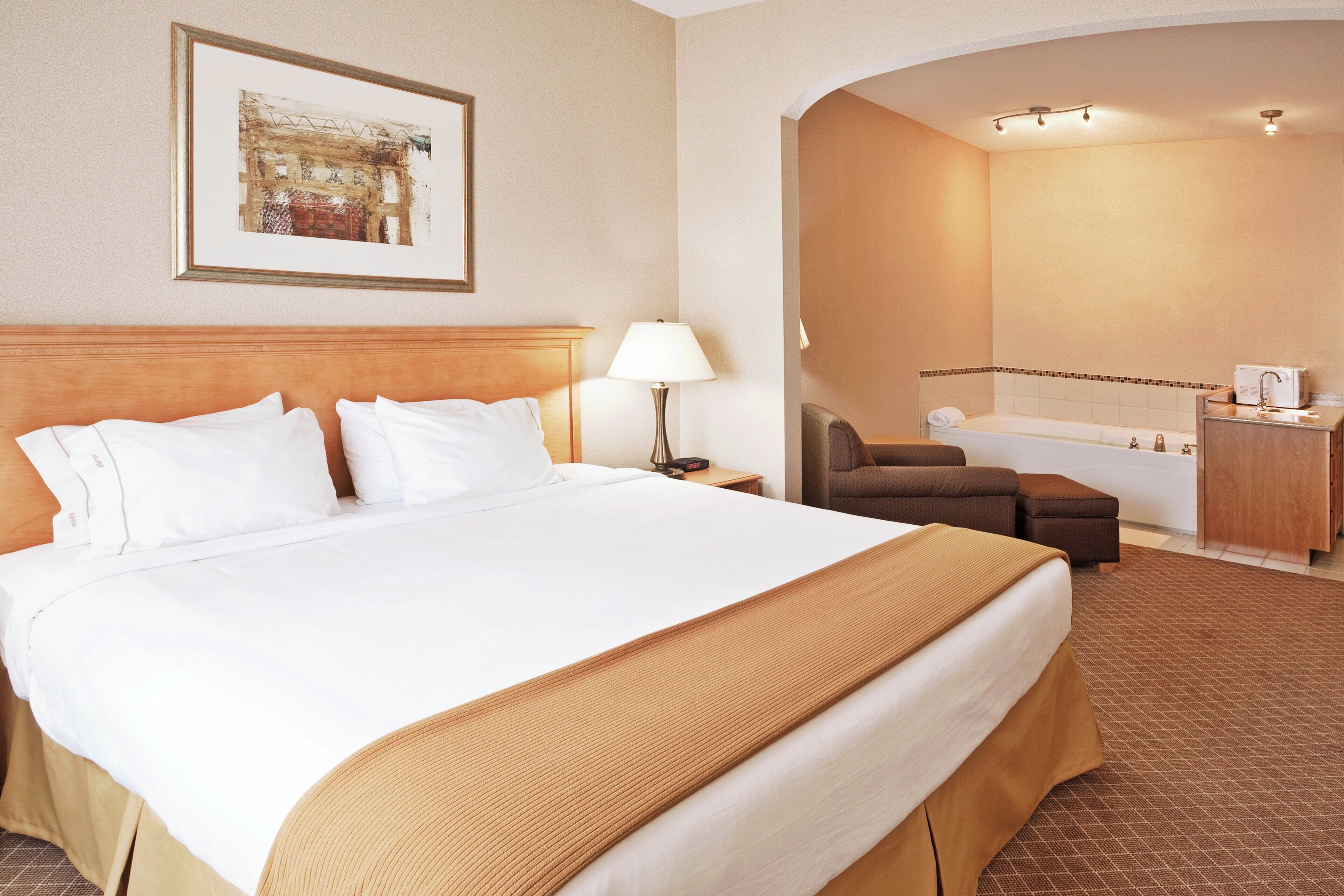 A hotel room with a large bed, a desk, a chair, a bathroom, and a framed picture on the wall.
