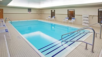 Una gran piscina interior con suelo de baldosas, un cartel de prohibición de saltos y varias sillas de descanso.