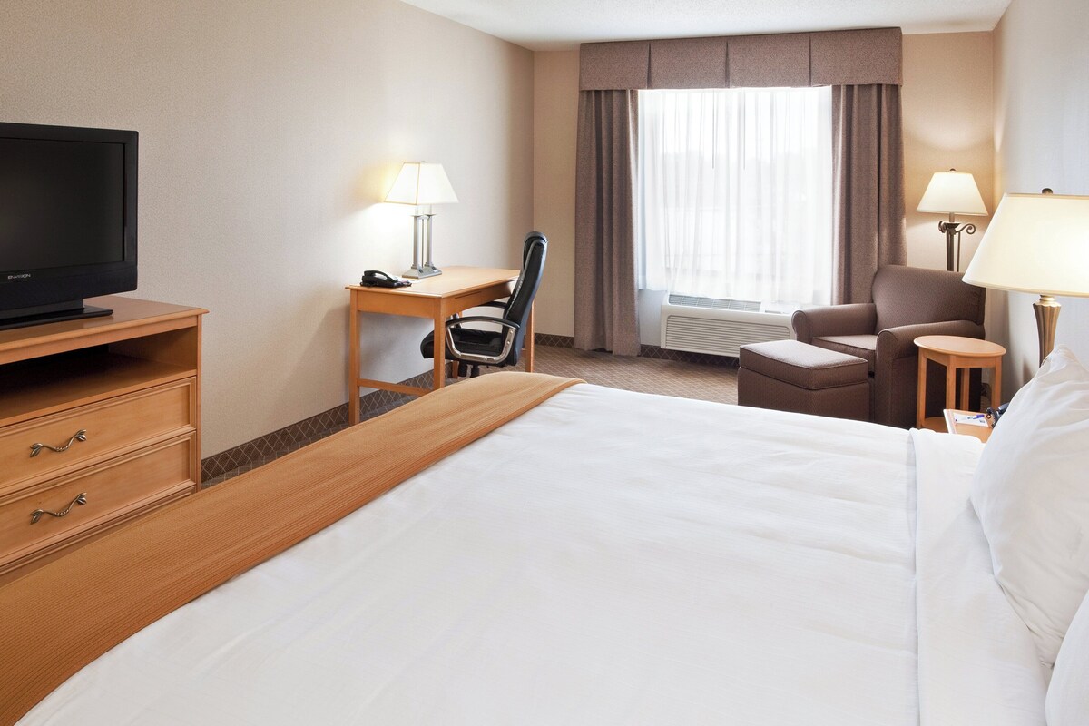 A hotel room with a bed, a desk, a chair, a television, and a window with curtains.