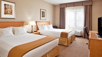 A hotel room with two beds, a desk, a chair, a TV, and framed artwork on the walls.