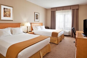 A hotel room with two beds, a desk, a chair, a TV, and framed artwork on the walls.