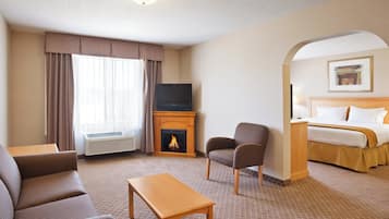 Habitació d'hotel amb una xemeneia, televisió, sofà, cadira, llit i una taula petita.