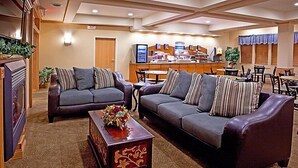 A hotel lobby with two sofas, a coffee table, a fireplace, a reception desk, and a dining area. - Holiday Inn Express & Suites Chesterfield by IHG (New Baltimore)