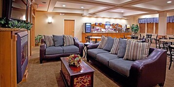 A hotel lobby with two sofas, a coffee table, a fireplace, a reception desk, and a dining area.
