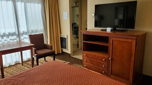 A hotel room with a bed, a TV on a wooden cabinet, a chair, a table, and a bathroom visible through an open door. - Royal Pacific Motor Inn (San Francisco)