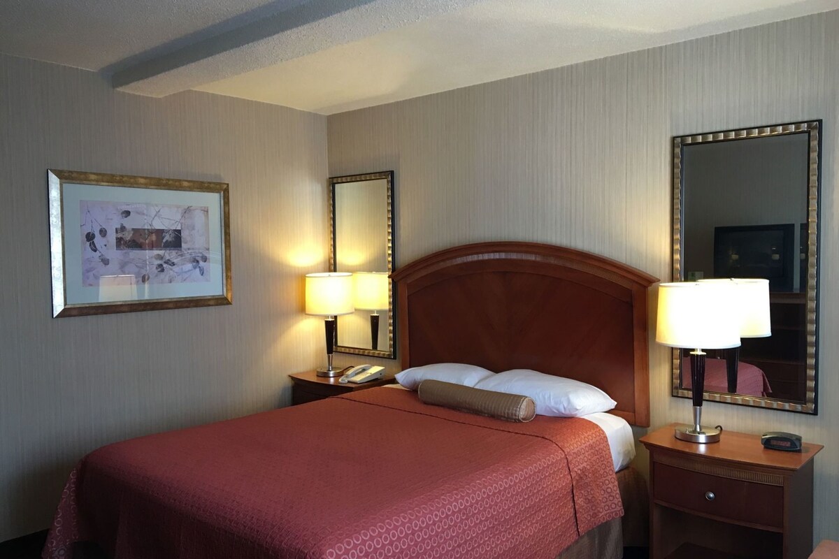A hotel room with a bed, two bedside tables, a nightstand, a mirror, and a framed picture on the wall.