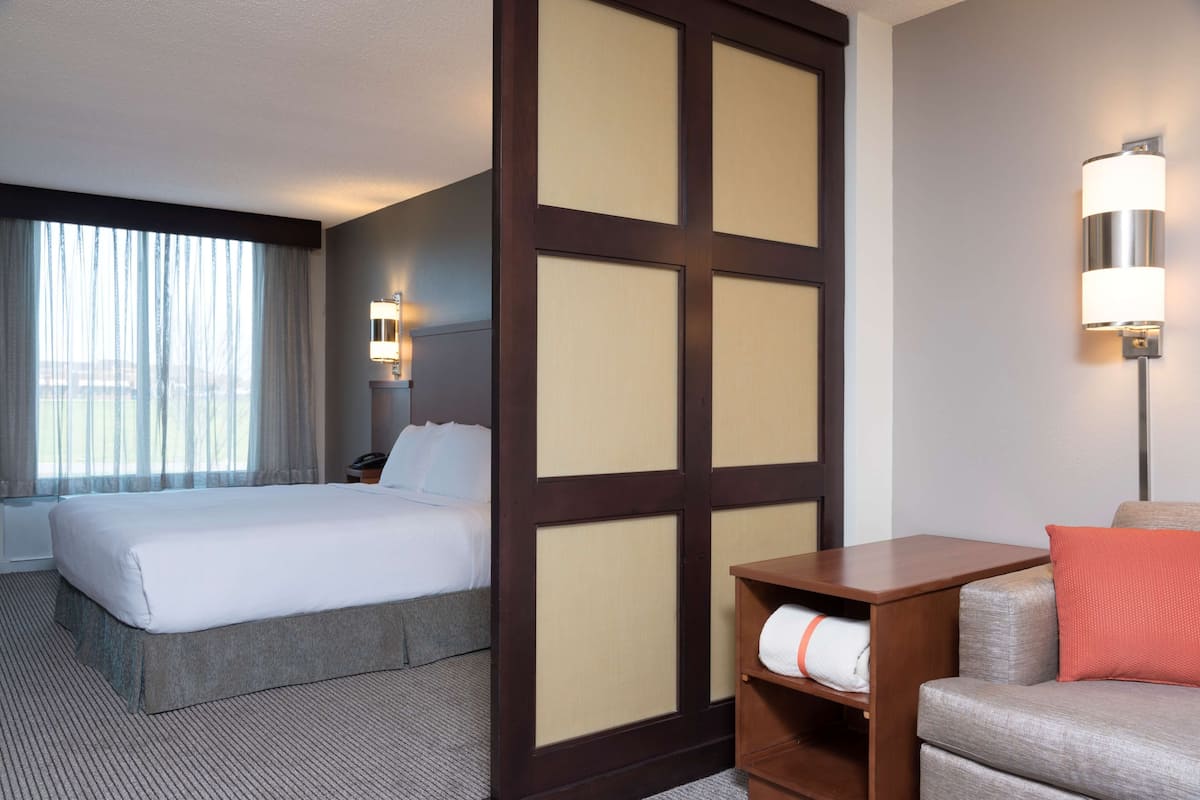 A hotel room with a large bed, a wooden nightstand, a lamp, and a sofa with a cushion.