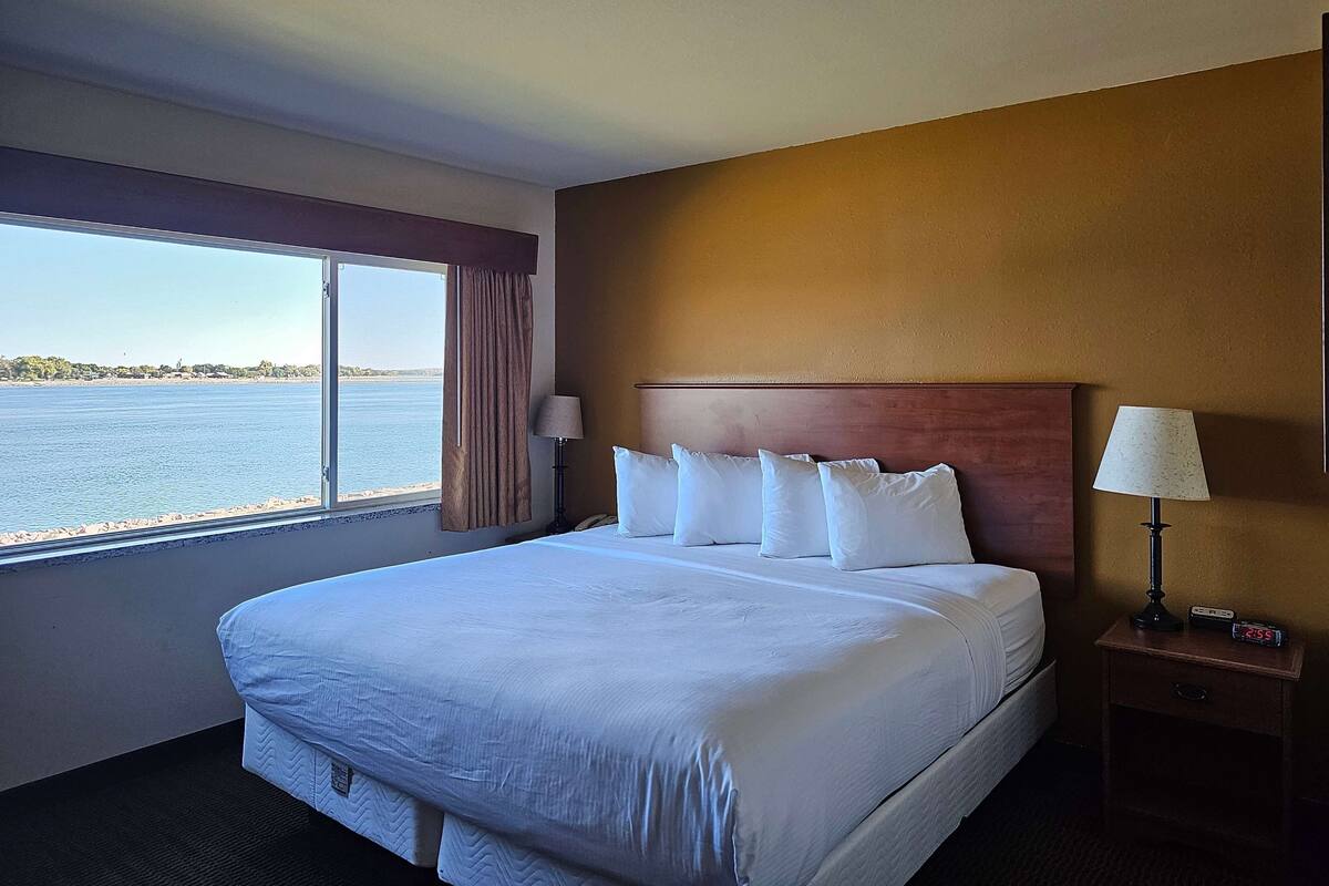 A hotel room with a large bed, a nightstand with a lamp, and a view of the water.