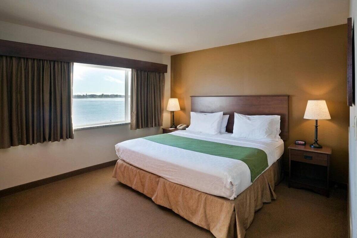 A hotel room with a large bed, two bedside lamps, a telephone, and a window with curtains.