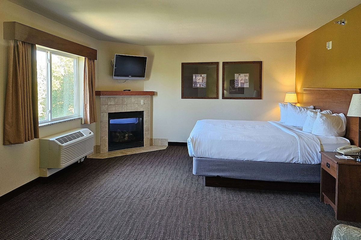 A hotel room with a bed, a television mounted above the fireplace, and two framed pictures on the wall.