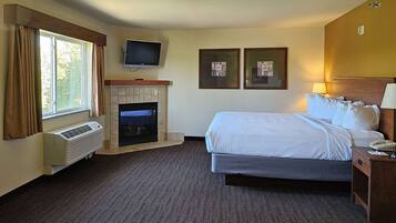 A hotel room with a bed, a television mounted above the fireplace, and two framed pictures on the wall.