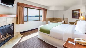 Ein Hotelzimmer mit einem Bett, einem Kamin, einem Fernseher, einem Fenster mit Blick auf das Wasser und einer Lampe.