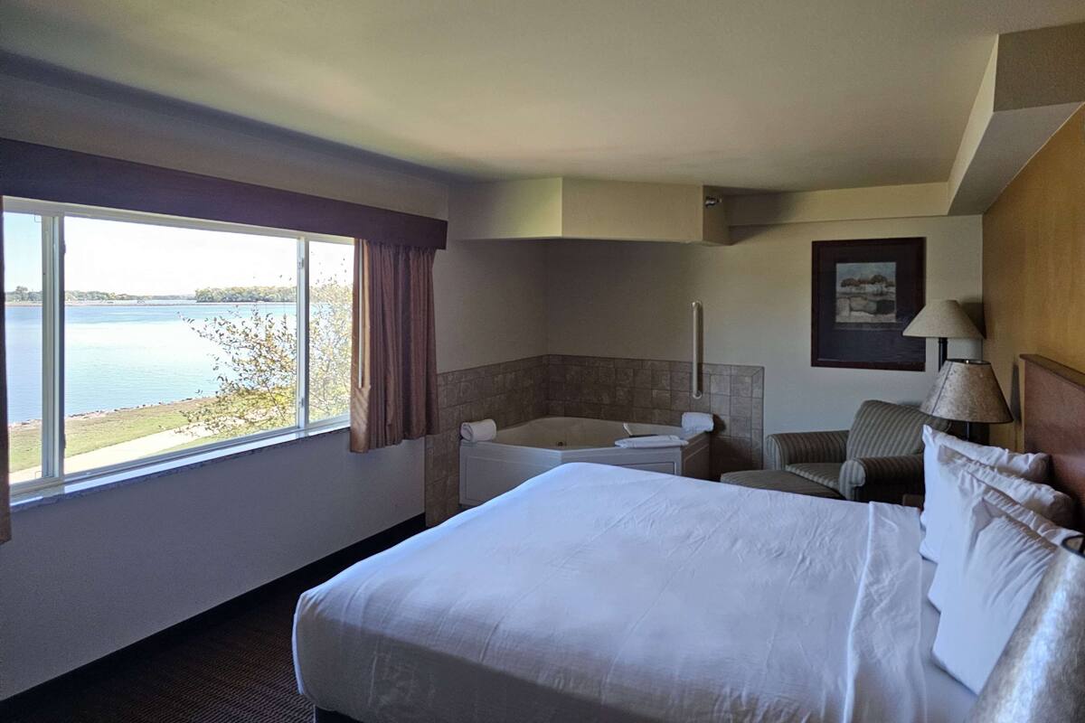 A hotel room with a large bed, a bathtub, a chair, and a view of a lake.