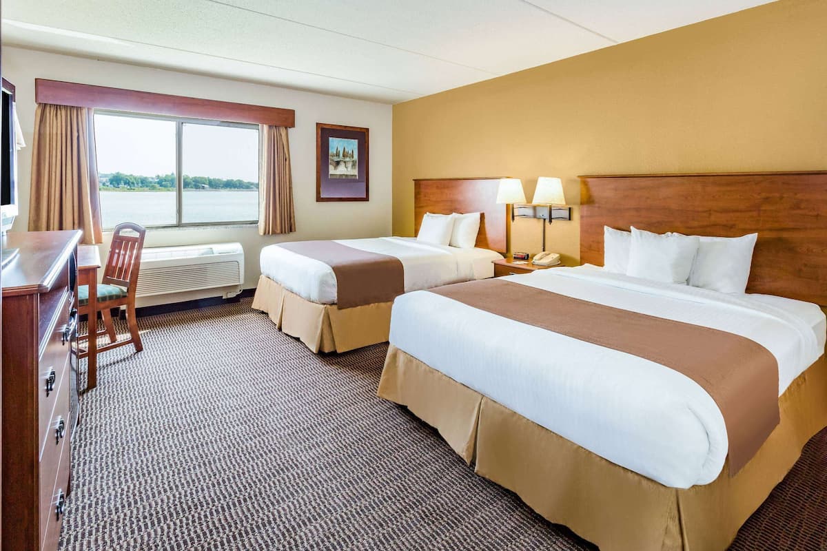 A hotel room with two beds, a desk, a chair, and a window with a view of a body of water.