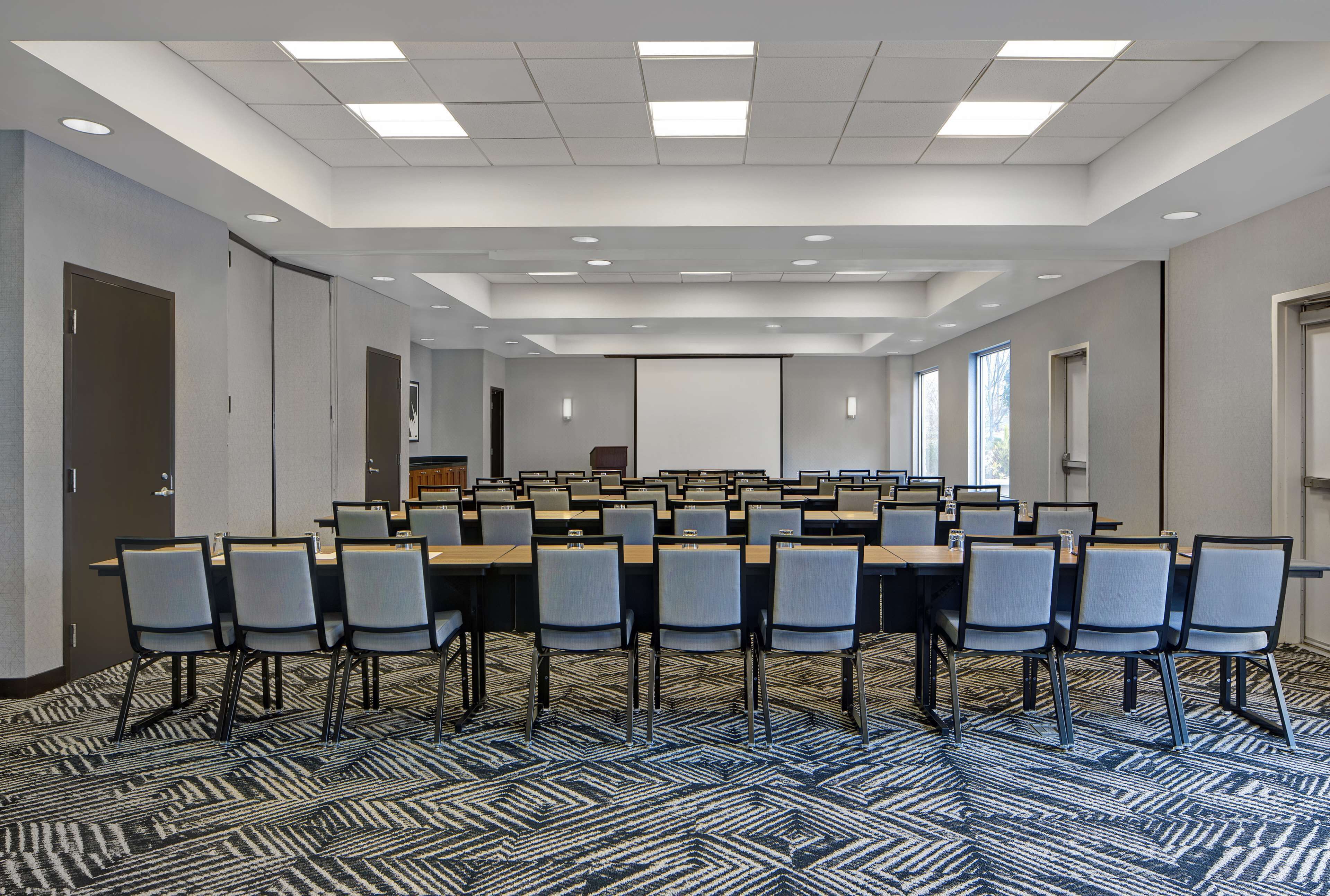 A conference room with a long table, multiple chairs, and a projector screen.