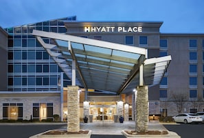 A Hyatt Place hotel entrance with a covered walkway, stone pillars, and a glass facade.