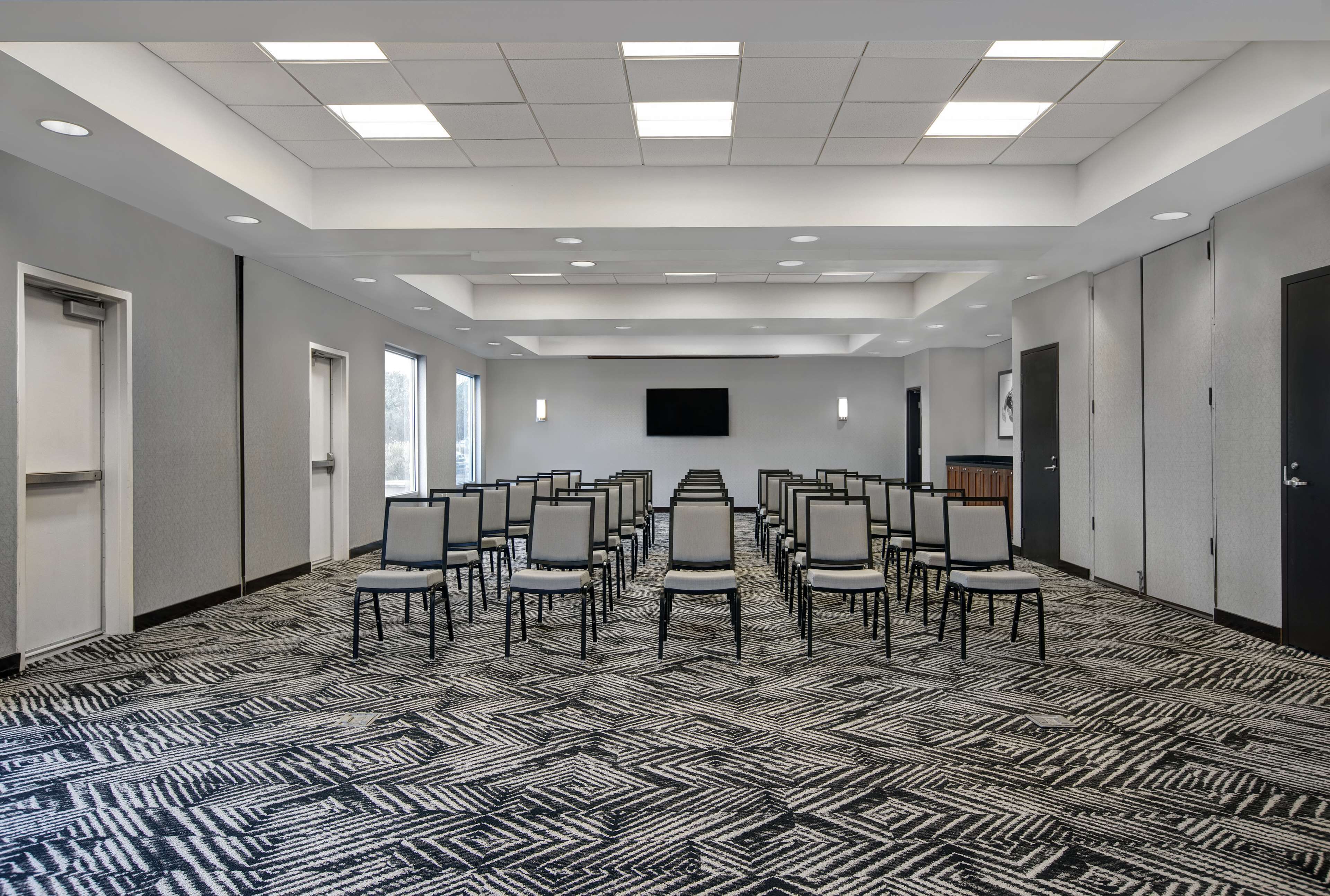 A conference room with rows of chairs, a flat-screen TV, and a patterned carpet.