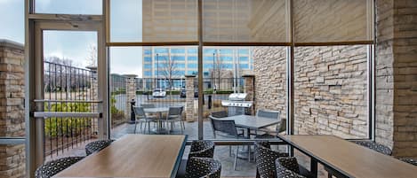An outdoor patio with tables and chairs, a stone wall, and a view of a building in the background.