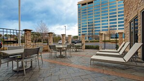 An outdoor patio with stone flooring, tables, chairs, and lounge chairs.