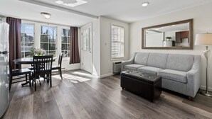 A modern living room with a grey sofa, a black ottoman, and a dining area with a table and chairs. - Pink Blossom Family Resort (Ogunquit)