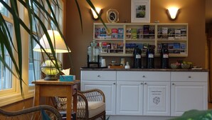 A kitchen with white cabinets, a wicker chair, a table with a lamp, and a bookshelf with various items. - Pink Blossom Family Resort (Ogunquit)