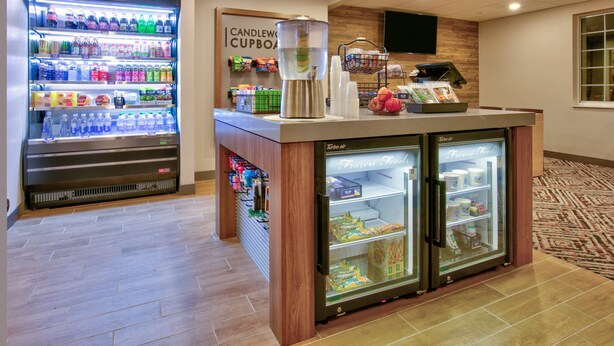 Un vestíbulo de hotel con una máquina expendedora de bebidas, una máquina de café y una vitrina refrigerada con alimentos congelados.