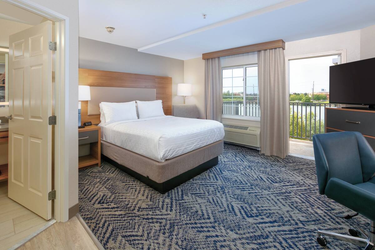 A hotel room with a large bed, a TV, a desk, and a view of the outside.