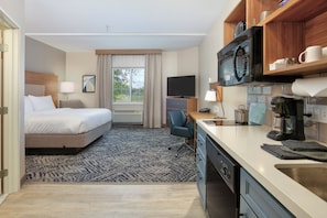 Habitación de hotel con cama, escritorio, microondas, cafetera y vistas al exterior.